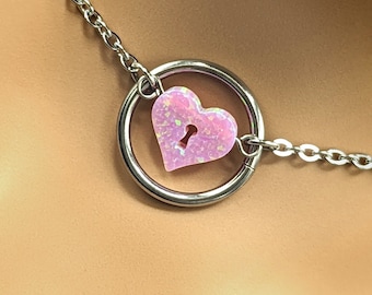 May include: A silver chain necklace with a pink heart charm featuring a keyhole. The heart charm is attached to a silver ring.