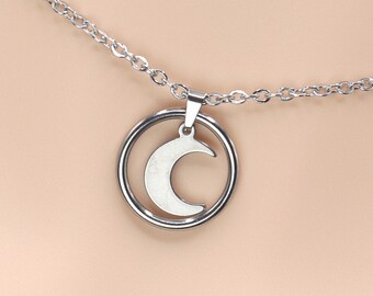 Puede incluir: Un collar de cadena de plata con un colgante que presenta una luna creciente dentro de un círculo.