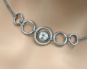 May include: A silver necklace with a chain and multiple circular links. The centre link features a clear crystal.