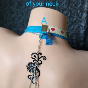 Puede incluir: Una cadena de cuerpo de plata con un dise&ntilde;o floral negro. La cadena se mide con una cinta m&eacute;trica, comenzando en el punto A en la base del cuello.