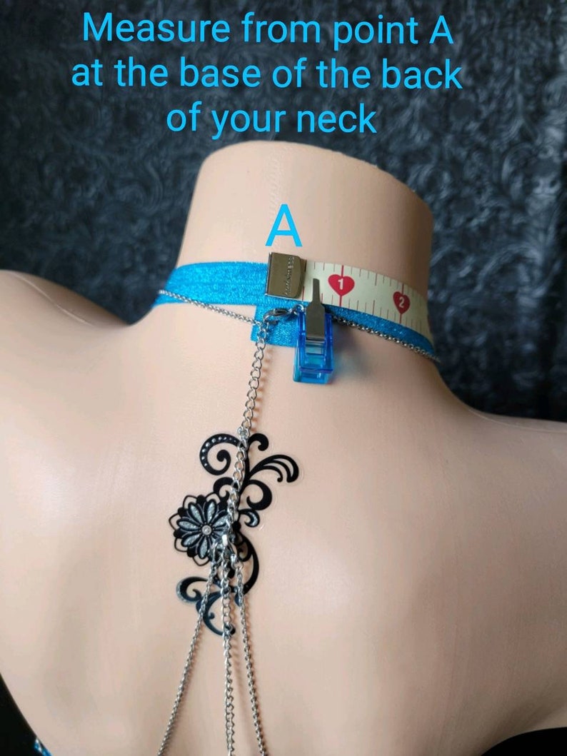 Puede incluir: Una cadena de cuerpo de plata con un dise&ntilde;o floral negro. La cadena se mide con una cinta m&eacute;trica, comenzando en el punto A en la base del cuello.