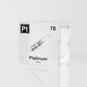 May include: A clear acrylic block displaying the element Platinum. The block features the symbol "Pt", atomic number 78, and the name "Platinum" with its atomic weight. A small glass vial containing platinum granules is embedded within.