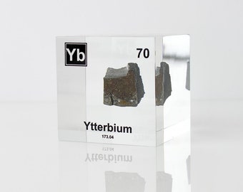 May include: A clear acrylic cube containing a small piece of Ytterbium, a silvery-white metal. The cube has the element's symbol "Yb", atomic number "70", and name "Ytterbium" printed on it.