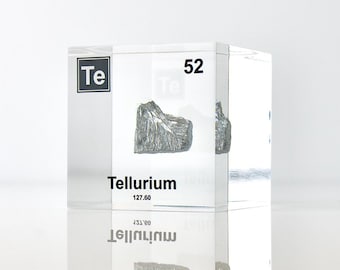 Op de afbeelding: Een doorzichtige acrylblokje met een monster van telluur. Het blokje is gelabeld met het symbool van het element "Te", het atoomnummer "52" en de naam "Telluur".