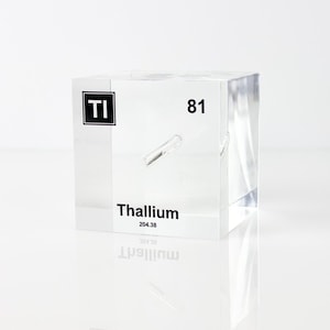May include: A transparent acrylic cube displaying the element symbol "TI" and the number "81". The word "Thallium" and its atomic weight are also printed on the cube. The cube is set on a white surface.