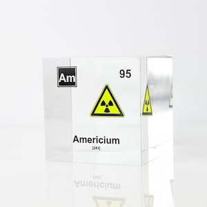May include: A clear acrylic cube displaying the chemical element Americium (Am). The cube shows the atomic number 95 and a yellow radiation warning symbol.