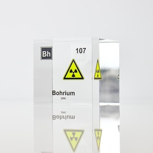 May include: A clear acrylic block displaying the chemical element Bohrium (Bh). The block features a yellow radiation warning symbol and the atomic number 107. The text "Bohrium" and the chemical symbol "Bh" are printed on the block.