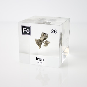 May include: A clear acrylic cube containing a small sample of iron metal. The cube has a label that reads "Fe" and "26" for the element's symbol and atomic number. The label also reads "Iron" and "55.845" for the element's name and atomic weight.