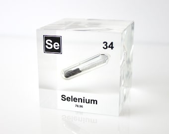 Op de afbeelding: Een heldere acryl kubus met het element Selenium. De kubus toont het symbool, het atoomnummer en het atoomgewicht van het element. Een kleine glazen buis met een Selenium monster is erin verwerkt. De kubus staat op een witte ondergrond.