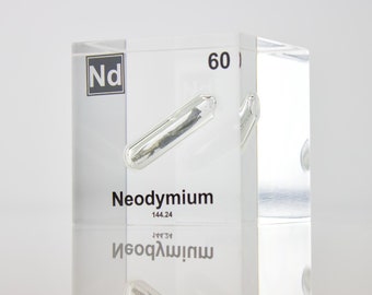 May include: A clear acrylic cube containing a small sample of neodymium metal. The cube has the chemical symbol Nd, the atomic number 60, and the atomic weight 144.24 printed on it. The word "Neodymium" is also printed on the cube.