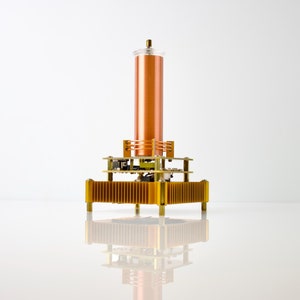 May include: A copper coil with a gold-colored base and a clear plastic top. The coil is mounted on a gold-colored circuit board with multiple components.