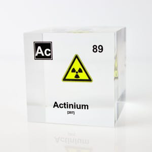 May include: A clear acrylic cube with the chemical symbol Ac, the number 89, and the word Actinium (207) printed on it. A yellow radiation warning symbol is also printed on the cube.