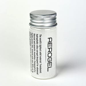 Op de afbeelding: Een heldere glazen flacon met een zilveren dop, gevuld met een witte, poederachtige substantie, met het label "AEROGEL". De tekst beschrijft het als 's werelds lichtste vaste materiaal.