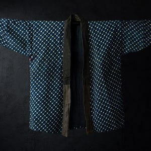 May include: A dark blue indigo jacket featuring a repeating white diamond pattern across the body and wide sleeves. The garment has a solid dark brown collar and a vertical striped panel along the front opening, creating a structured silhouette.