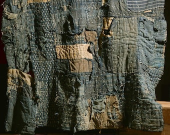 May include: A large patchwork quilt made of blue and white fabric. The quilt is made of many different pieces of fabric, some of which are faded and worn. The quilt is hanging on a wooden wall.