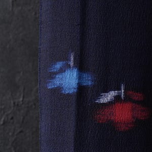 Puede incluir: Primer plano de una tela azul marino con un tejido texturizado. La tela presenta diseños abstractos en azul, rojo y blanco. Los diseños parecen pinceladas o elementos pintados, agregando interés visual al textil.