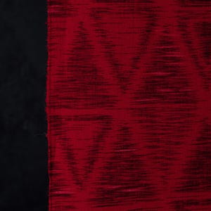 May include: A piece of fabric featuring a deep red color with a dark, horizontal, brushstroke-like texture. The material displays a repeating geometric diamond pattern created by variations in the density of the dark red and black fibers.