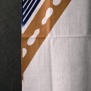Puede incluir: Tela blanca con un diseño diagonal en tonos marrón, azul marino y blanco. El diseño incluye una franja marrón con detalles blancos en forma de lágrima y una sección azul marino con rayas blancas. La tela tiene una apariencia texturizada.