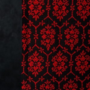 May include: A fabric featuring a repeating pattern of bright red floral motifs arranged within a black hexagonal grid. The design consists of symmetrical, stylized blossoms and leaves that create a continuous, interconnected geometric layout.