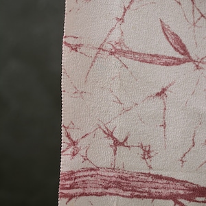 Puede incluir: Primer plano de una tela con fondo crema y un patrón abstracto granate, similar a venas. La tela tiene una superficie texturizada y un borde sin rematar a la derecha. El patrón se asemeja a una red de ramas.