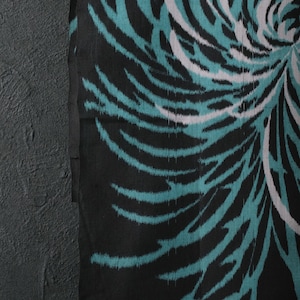 May include: A close-up of a textile with a black backdrop and a large, stylised floral pattern. The design features teal, white, and magenta curved lines radiating from a central point. The fabric has a textured appearance, creating a dynamic visual effect.