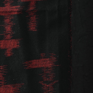 Puede incluir: Primer plano de un textil negro con un patrón abstracto rojo. El diseño presenta formas horizontales y verticales similares a pinceladas. La tela tiene una apariencia texturizada, con un borde negro sólido en el lado derecho. Este textil podría usarse para ropa o decoración del hogar.