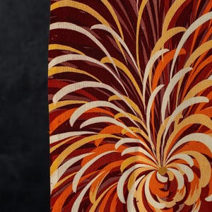 May include: A piece of fabric featuring a vibrant, abstract floral pattern with sweeping, curved lines in shades of deep burgundy, bright orange, golden yellow, and cream. The design radiates from a central point, creating a dynamic, layered effect across the textured surface of the textile material.