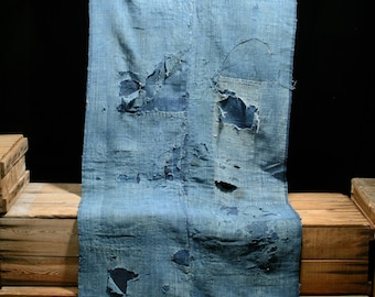 May include: A long, blue, indigo-dyed fabric with several patches and holes. The fabric is folded and draped over a wooden surface.