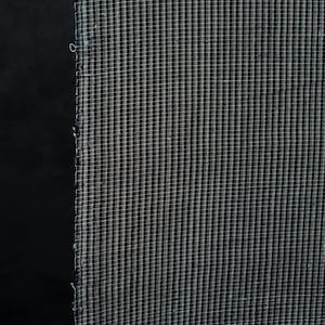 Könnte beinhalten: Ein Stück Stoff mit einem dichten, sich wiederholenden Mikro-Karomuster in Dunkelmarineblau und Weiß. Das Textil weist eine sichtbare Webstruktur auf, mit einer leicht ausgefransten, rohen Kante, die vertikal an der linken Seite verläuft.