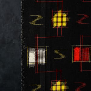 May include: A black fabric featuring a repeating pattern of small, square-shaped blocks in white, yellow, and red. Each block is outlined by thin, intersecting red lines, and the design includes small, horizontal, zigzag-like shapes in red.