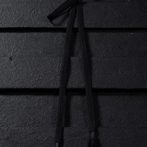 Puede incluir: Un cordón negro con borlas en cada extremo. El cordón está sobre una superficie de madera negra.