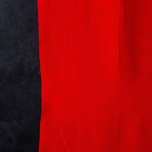 May include: A vertical image featuring a vibrant red fabric panel next to a dark, textured black panel. The red fabric has a slightly textured appearance, while the black panel has a rough, almost suede-like texture.