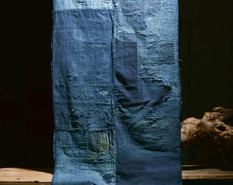 May include: A blue indigo fabric with patches of different shades of blue. The fabric has a worn and distressed look, with frayed edges and visible stitching.