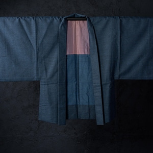 May include: A blue haori jacket with wide sleeves and a structured collar. The garment features a solid blue exterior fabric and a contrasting light pink lining visible at the inner neck and upper back area, hanging open on a horizontal rod.