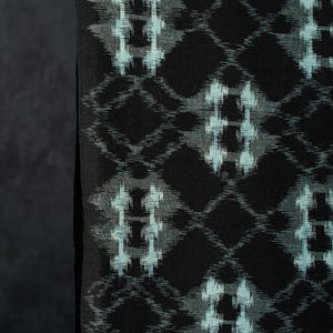 May include: A black fabric featuring a repeating diamond-shaped pattern in light blue and grey. The design consists of interconnected geometric shapes with a soft, blurred edge effect, creating a consistent grid across the dark textile surface.