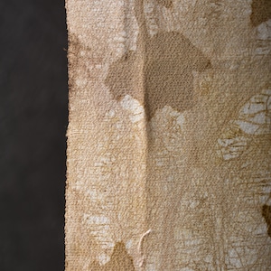 Puede incluir: Primer plano de una tela texturizada con un patrón beige y marrón. La tela tiene un aspecto rugoso y tejido con formas irregulares y un fondo oscuro en el lado izquierdo.