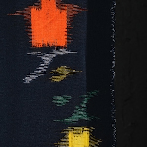 Pode incluir: Close-up de um tecido azul escuro com um padrão repetido de formas abstratas em laranja, amarelo, verde e branco. As formas têm uma aparência pixelizada, criando um efeito texturizado. A borda do tecido é visível à direita.