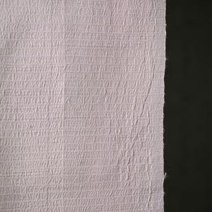 Könnte beinhalten: Nahaufnahme eines strukturierten, hellvioletten Stoffes. Der Stoff hat ein gewebtes Aussehen mit einem subtilen, sich wiederholenden Muster. Der rechte Rand des Stoffes ist roh und unfertig, vor einem dunklen Hintergrund.