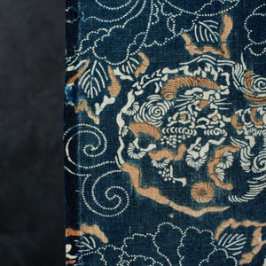 Puede incluir: Un tejido de color azul profundo con un patrón denso y complejo de contornos florales punteados en blanco y formas orgánicas de color tostado. La tela muestra un motivo repetitivo de flores estilizadas y líneas onduladas.