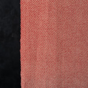 Op de afbeelding: Een stuk stof met een strak, uniform weefsel en een levendig rood en wit kleurenpalet. Het materiaal vertoont een consistent, kleinschalig geometrisch patroon dat wordt gecreëerd door het verweven van rode en witte draden over het oppervlak.