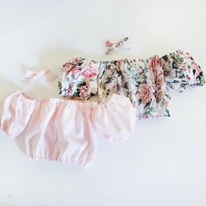 May include: Two off-the-shoulder tops with floral patterns. One top is pink and the other has a white background with pink and green flowers.