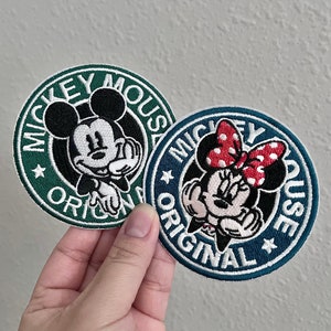 May include: Two embroidered iron-on patches featuring Mickey Mouse and Minnie Mouse. The patches are circular and have a green and blue background with white text that reads "Mickey Mouse Original".