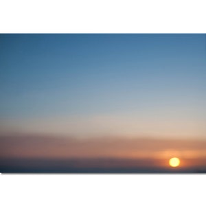 May include: A blurry sunset with a bright orange sun in the sky. The sky is a gradient of blue, pink, and orange.