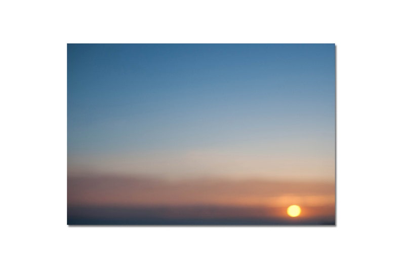 May include: A blurry sunset with a bright orange sun in the sky. The sky is a gradient of blue, pink, and orange.