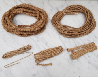 May include: Several coils of natural brown rope are arranged on a white surface. Two large coils are at the top, with smaller coils and a looped section below. The rope appears to be made of a coarse, fibrous material.