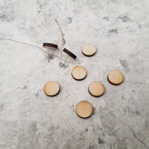 May include: A set of six wooden earrings in a light brown color. The earrings are round and have a simple design. They are displayed on a light gray surface.