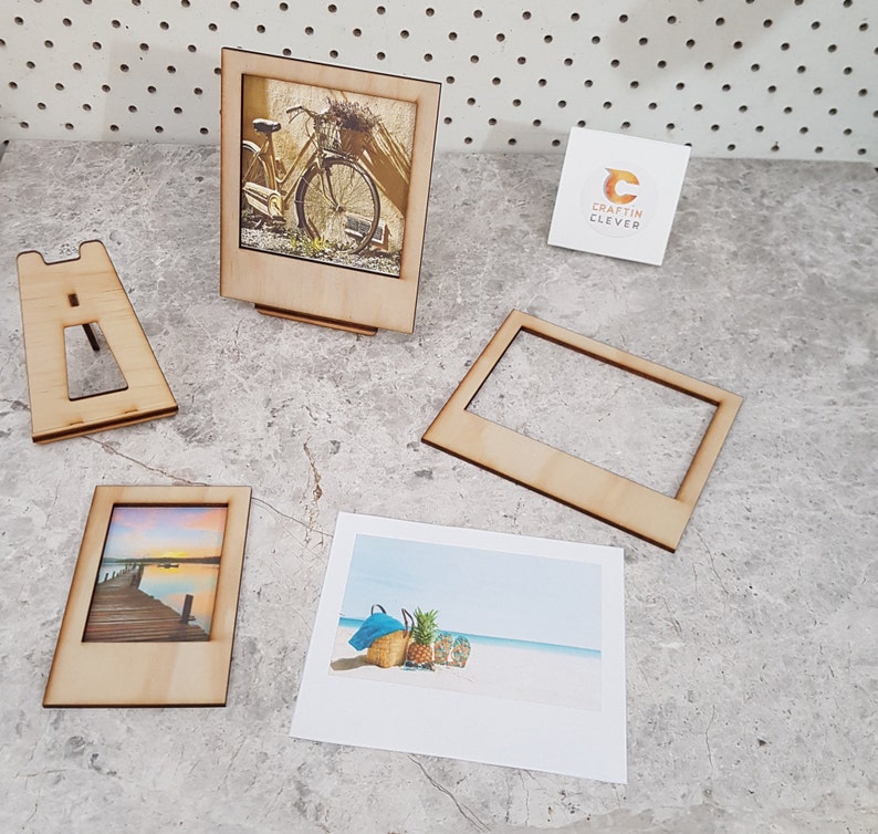Peut inclure: Un ensemble de quatre cadres photo en bois avec un fond blanc et une finition en bois clair. Les cadres sont en forme d'appareil photo instantan&eacute; Polaroid. Les cadres sont de tailles diff&eacute;rentes et sont dispos&eacute;s en rang&eacute;e sur une surface gris clair. Les cadres sont parfaits pour afficher des photos ou des &oelig;uvres d'art.