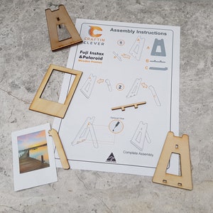 Peut inclure: Instructions de montage pour un cadre en bois pour photos Fuji Instax et Polaroid. Les instructions montrent comment assembler le cadre &agrave; l'aide de deux morceaux de bois &eacute;tiquet&eacute;s A, un morceau &eacute;tiquet&eacute; B et un morceau &eacute;tiquet&eacute; C. Les instructions montrent &eacute;galement un cadre termin&eacute; avec une photo ins&eacute;r&eacute;e.