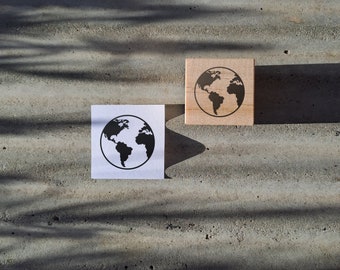 May include: Two wooden blocks with a black and white image of the Earth on each. One block is on a white card and the other is on a gray surface.