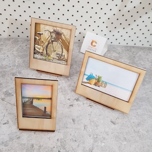 Peut inclure: Trois cadres photo en bois avec des images diff&eacute;rentes. Le premier cadre a une image d'un v&eacute;lo vintage avec un panier de fleurs. Le deuxi&egrave;me cadre a une image d'une sc&egrave;ne de plage avec un sac de plage bleu, des ananas et des tongs. Le troisi&egrave;me cadre a une image d'un coucher de soleil sur un lac avec une jet&eacute;e en bois.